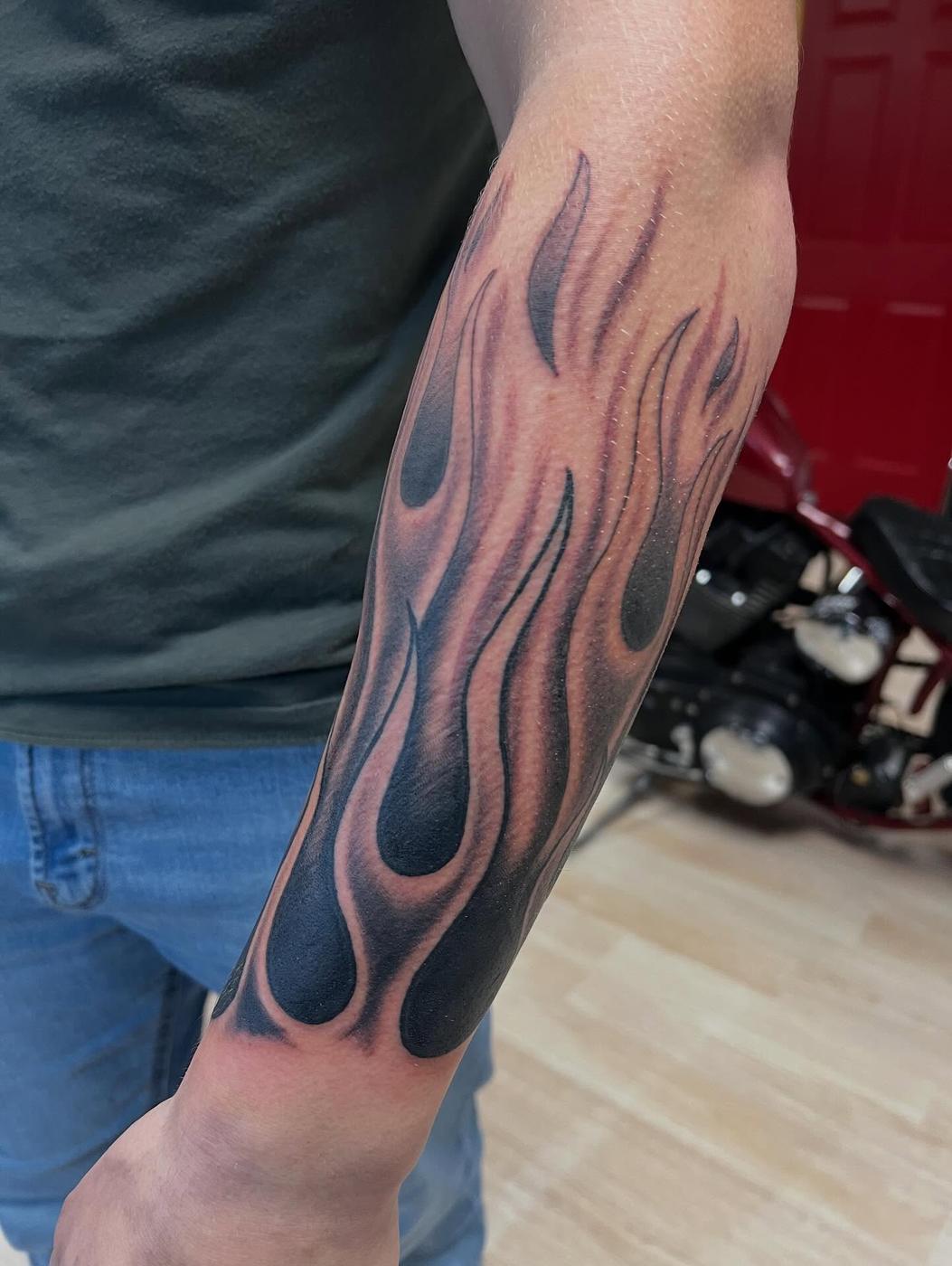 A black and gray flames tattoo wrapping a forearm