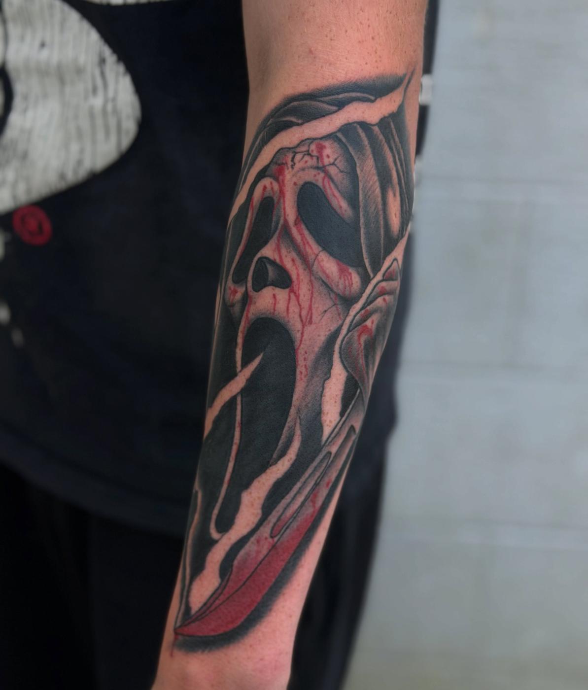 A black work horror mask tattoo on a forearm