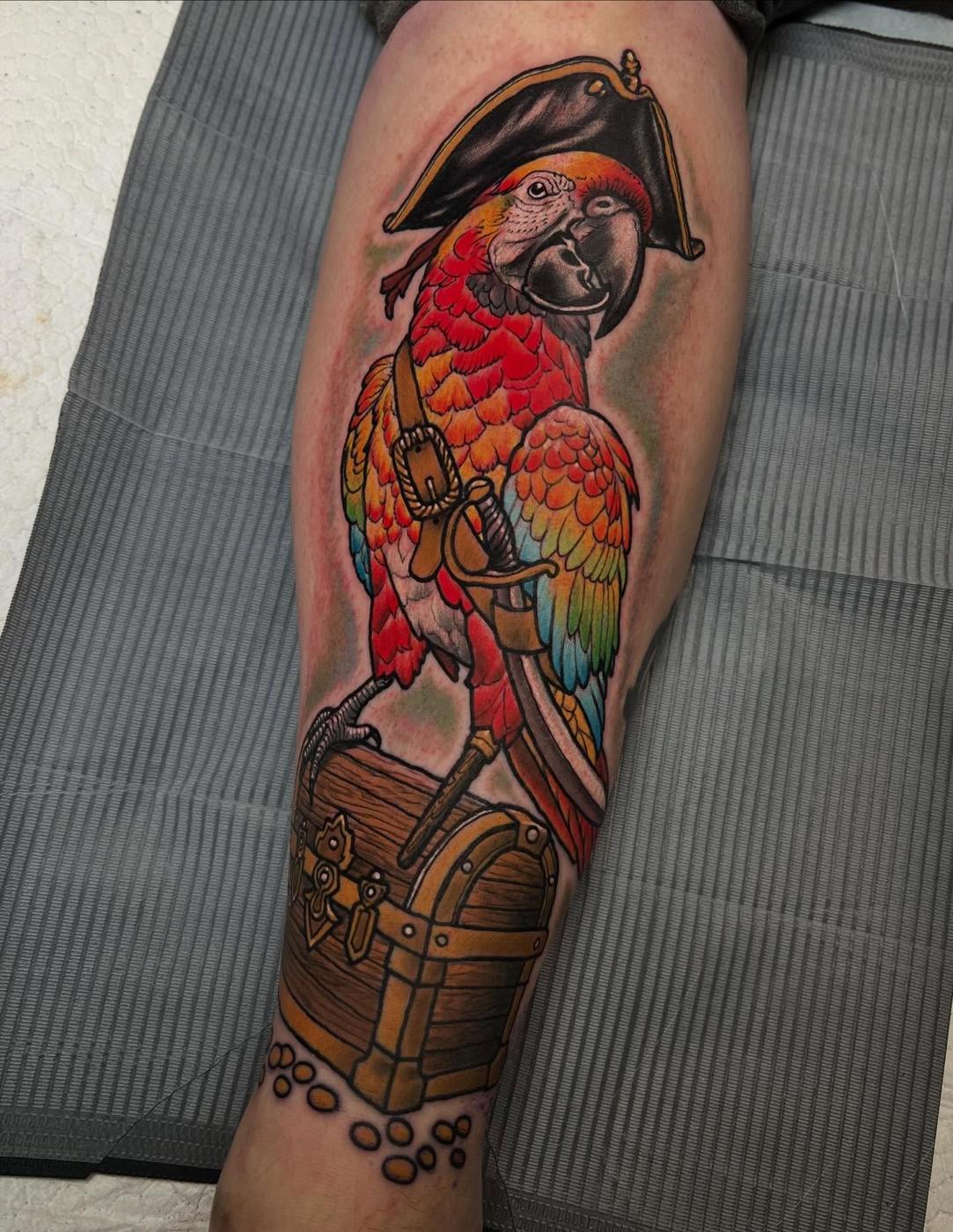 A color parrot and treasure chest tattoo on a leg