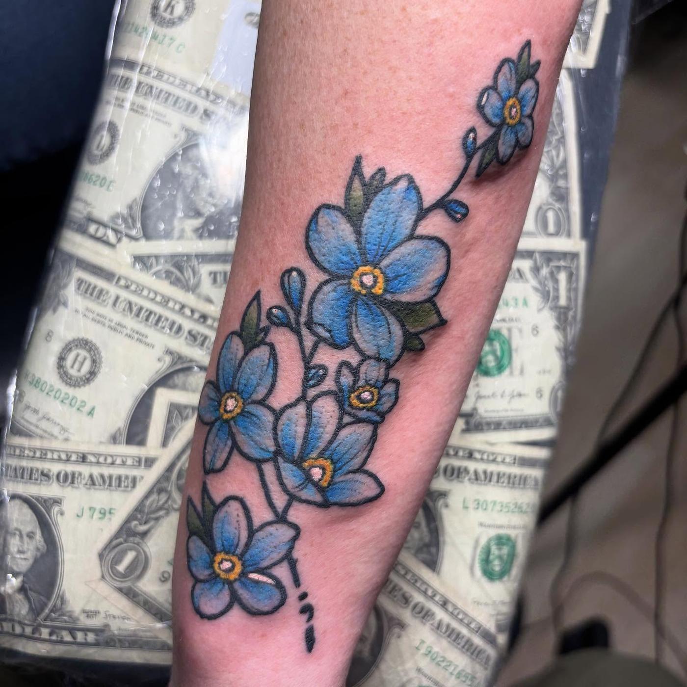 Small blue forget me not flowers tattooed along a forearm
