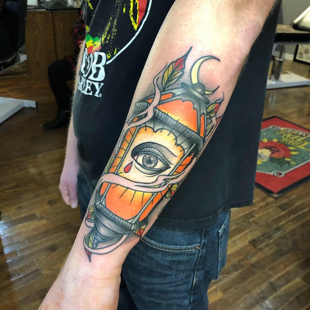 A color tattoo of an eye inside a lantern on a forearm
