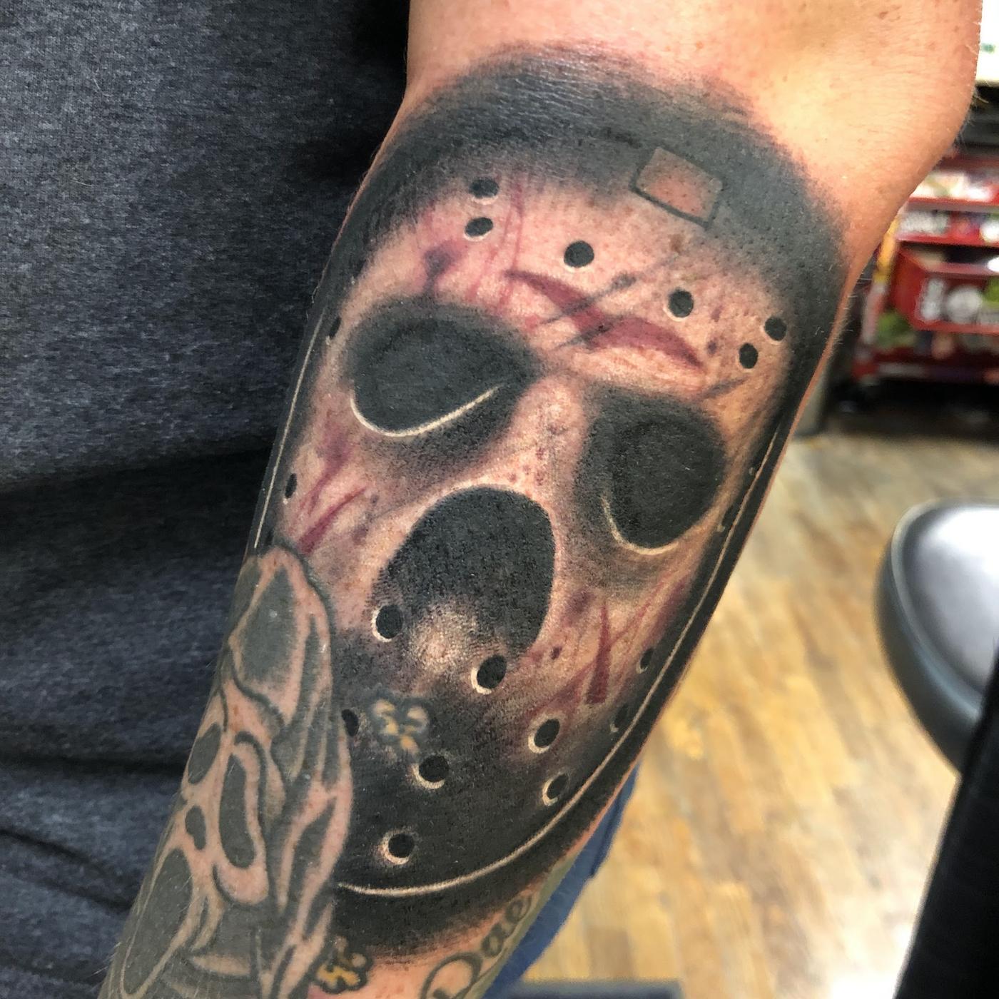 A black and gray horror mask tattoo on an arm