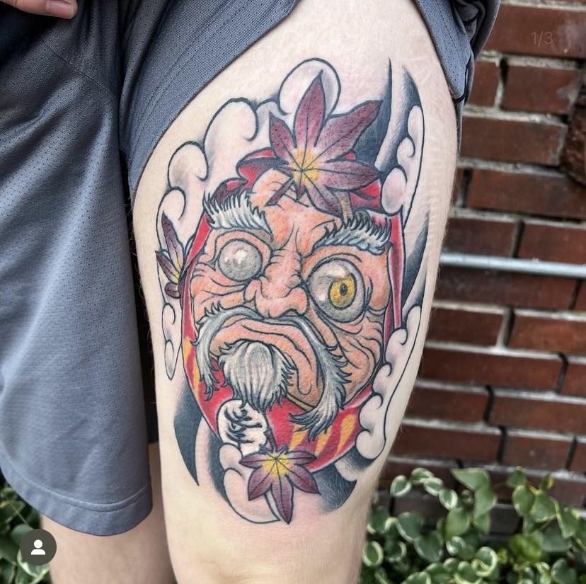 A color Japanese style mask tattoo with maple leaves on a thigh